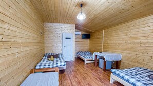 Una habitación pequeña con paredes y suelos de madera, que incluye dos camas, una mesita y un televisor.