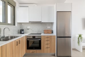 Een moderne keuken met witte kasten, een roestvrijstalen koelkast, een inbouwoven en een marmeren aanrecht.