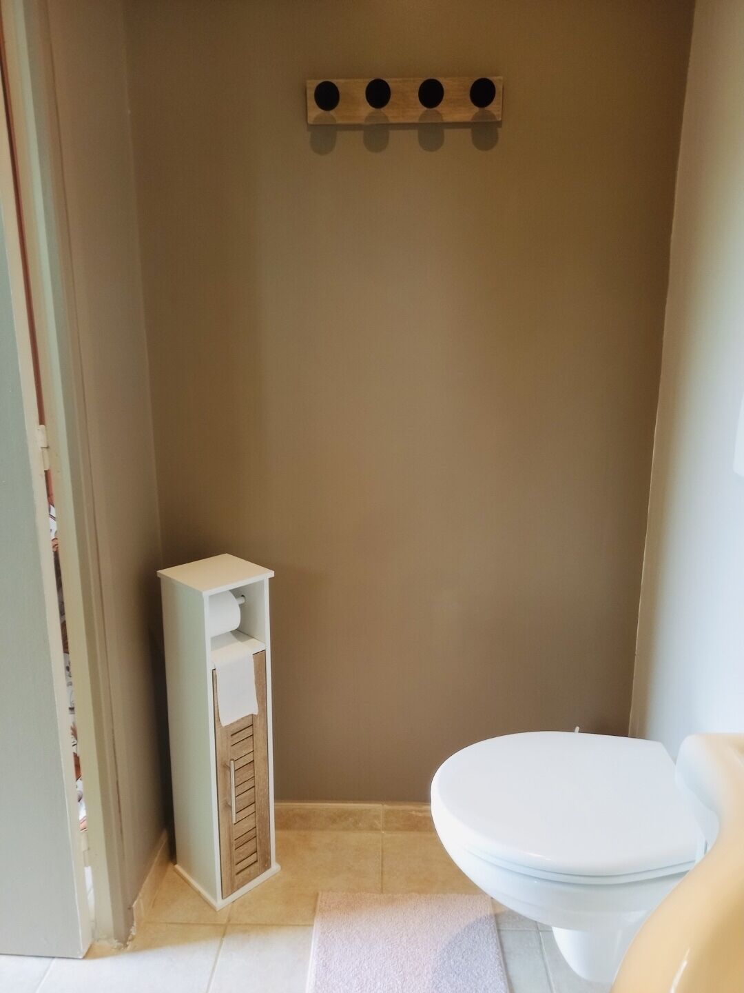 Een badkamer met een toilet, een klein kastje en een handdoekhouder aan de muur.