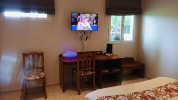 A room with a bed, a desk with a computer, a chair, and a television mounted on the wall.