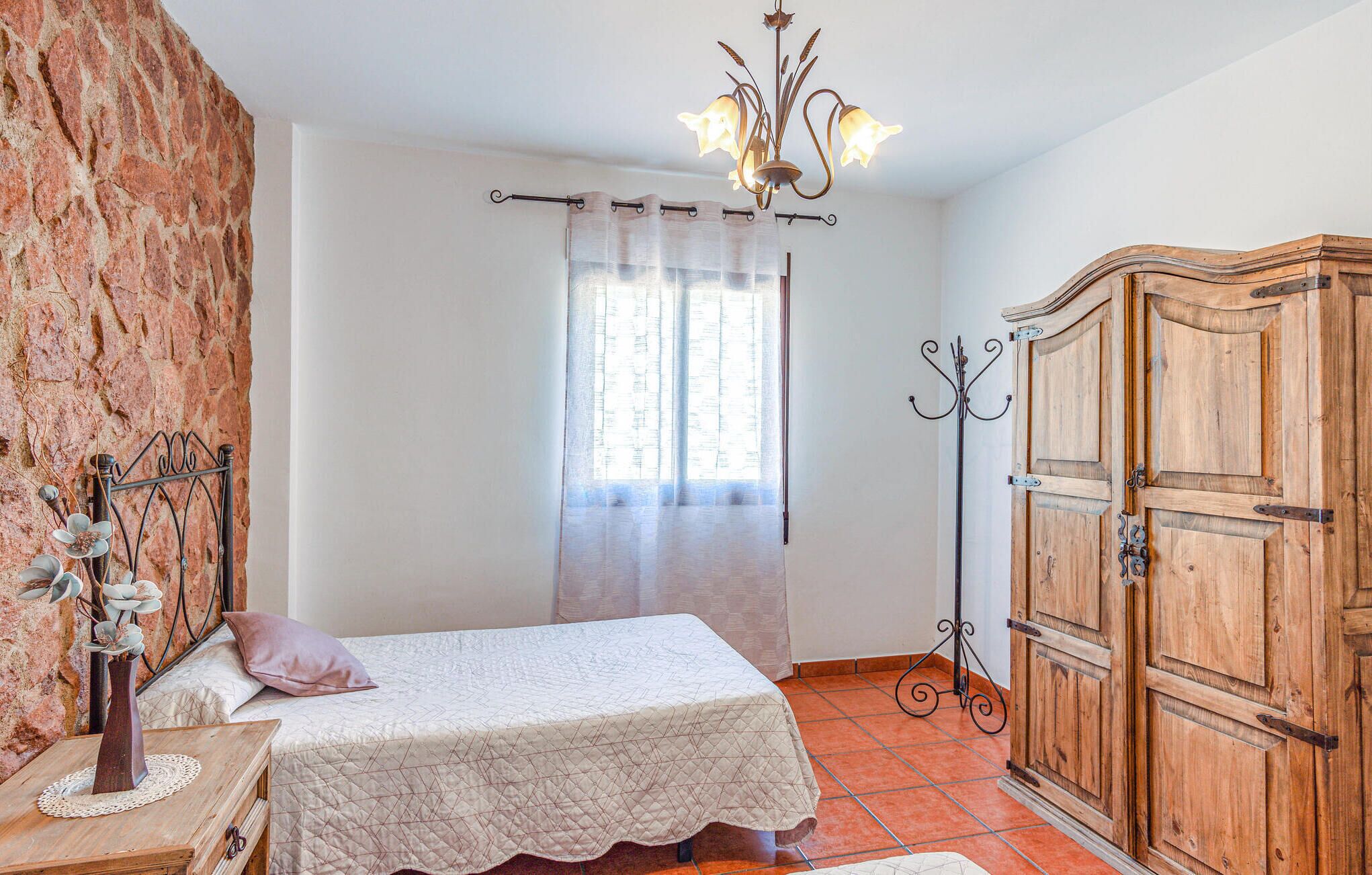 Ein Schlafzimmer mit Bett, einem Holzschrank, einer Chandelier und einer rustikalen Wand.