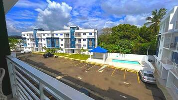 A multi-story building with a pool, parking lot, and a view of a street with cars.