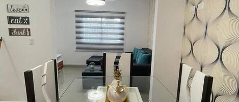 Een moderne eetruimte met een glazen tafel en zwarte stoelen, een decoratieve ananas als middelpunt en een muur met een geometrisch patroon.