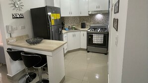 A modern kitchen with white cabinets, a black refrigerator, a gas stove, and a small island with bar stools. - Apartamento en moca (Moca)