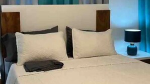A neatly made bed with white bedding, a wooden headboard, and a bedside table with a lamp. - Apartamento en moca (Moca)