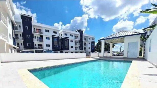 A swimming pool with a clear blue water, surrounded by a white tiled deck. - Apartamento en moca (Moca)