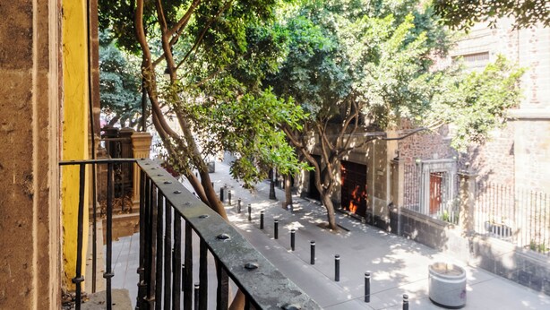 A courtyard with a stone bench, a metal railing, and trees. - Colmena Hotel CDMX Centro (Mexico City)