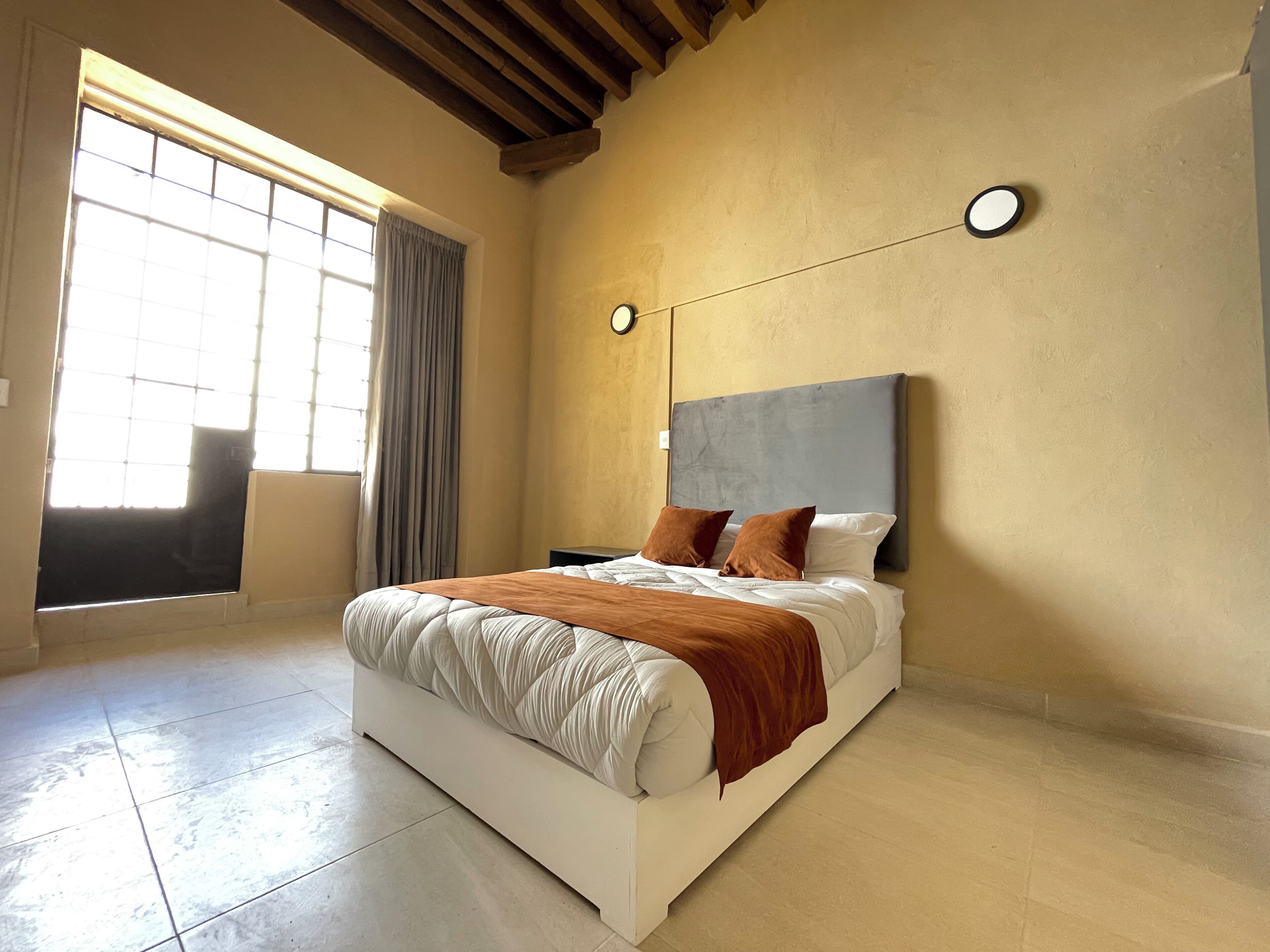 A bedroom with a bed, a window with curtains, a clock on the wall, and a tiled floor.