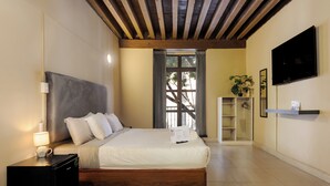 A bedroom with a bed, bedside table, lamp, TV, and a window with curtains. - Colmena Hotel CDMX Centro (Mexico City)