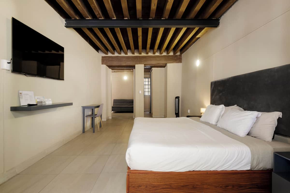Un dormitorio con cama, televisor montado en la pared, mesita de noche y una silla.