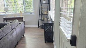A living room with a grey sofa, a small table with decorative items, a ladder shelf with plants, and a door with a window. - Alan's Apartment - Hot tub, fireplace, located in a quiet corner of Helen. (Helen)