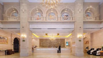 A grand lobby with a reception desk, high ceilings, and a chandelier.