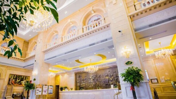 A grand lobby with a high ceiling, chandeliers, a reception desk, and a large mural. - Vienna International Hotel (Xinhua)