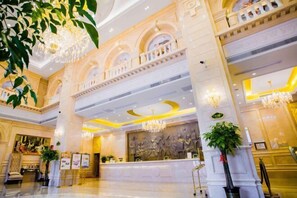 A grand lobby with a high ceiling, chandeliers, a reception desk, and a large mural. - Vienna International Hotel (Xinhua)