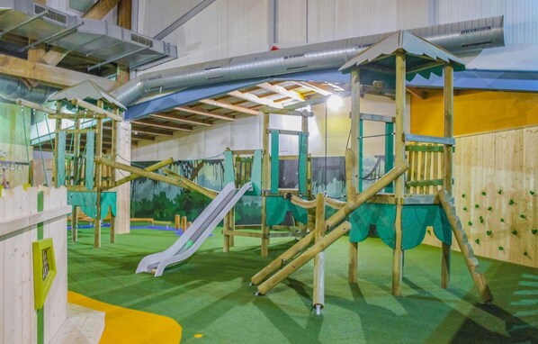An indoor play area with a slide, climbing structures, and a covered playhouse.