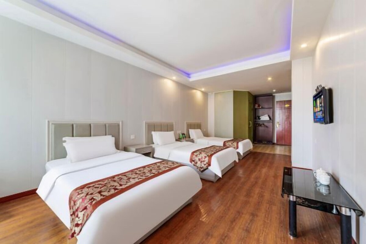 Habitación de hotel con tres camas, una mesita pequeña y un televisor en la pared.