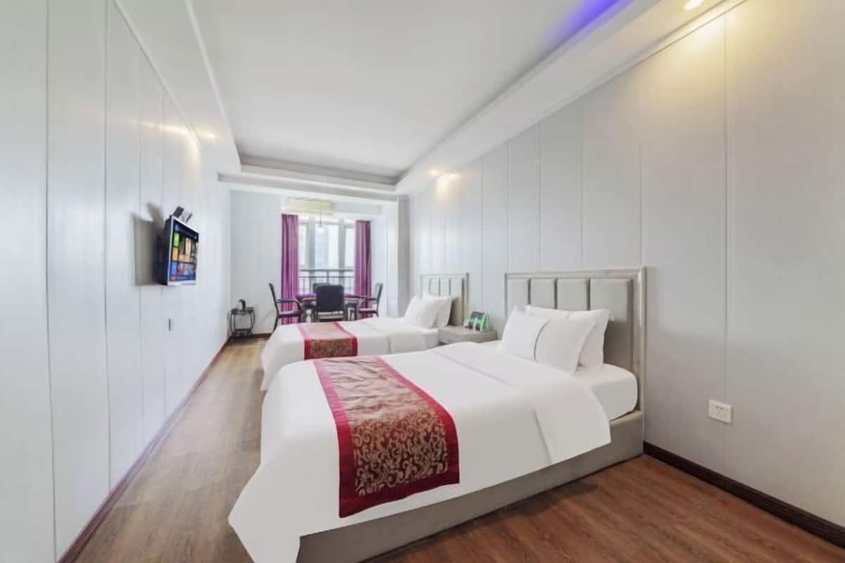 A hotel room with two beds, a TV, and a desk with a chair.