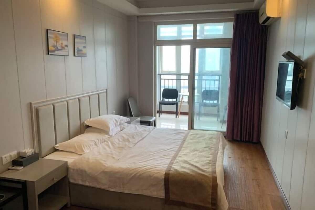 A hotel room with a bed, a nightstand, a TV mounted on the wall, and a balcony with a chair.