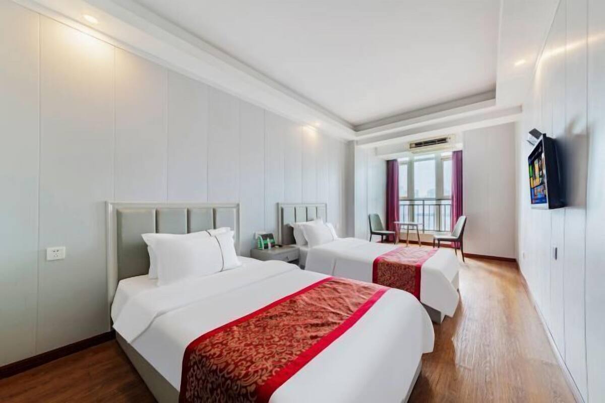 A hotel room with two beds, a television, and a window with curtains.