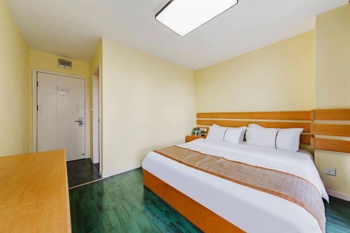 A hotel room with a large bed, wooden headboard, and a bedside table.