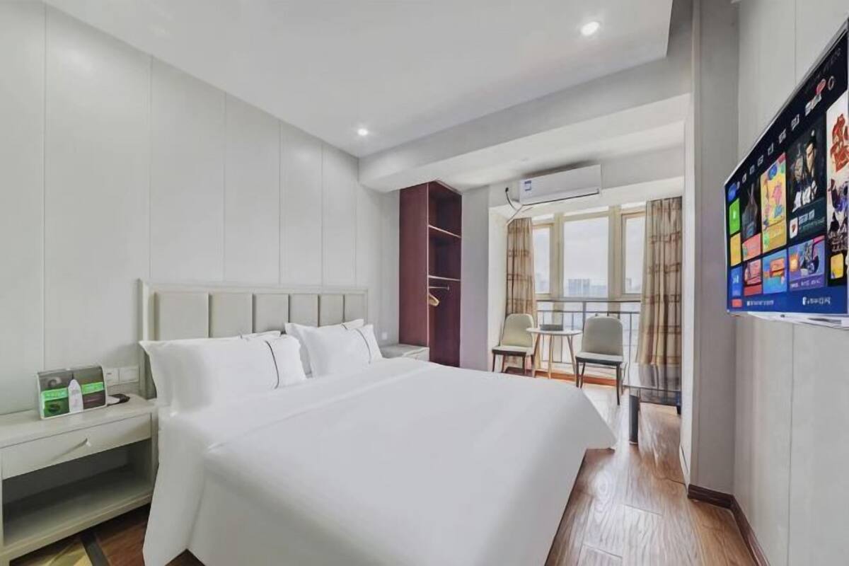 A hotel room with a large bed, a desk, a wardrobe, and a TV mounted on the wall.