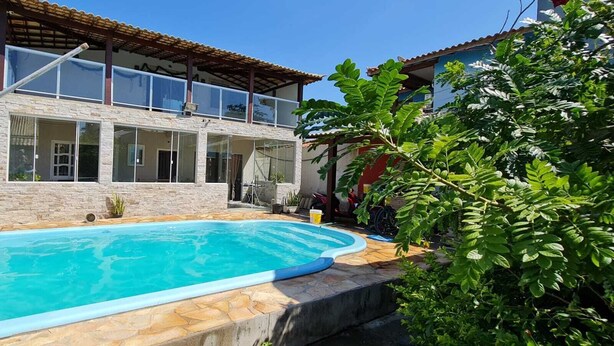 A swimming pool with a stone deck, surrounded by a house with large windows and a tiled roof. - Casa Shalom Buzios Official (Armação dos Búzios)