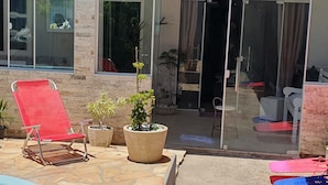 A poolside area with a red lounge chair, potted plants, and a glass door leading to an outdoor seating area. - Casa Shalom Buzios Official (Armação dos Búzios)