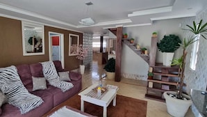 A living room with a purple sofa, a coffee table, and a staircase leading to a second floor. - Casa Shalom Buzios Official (Armação dos Búzios)