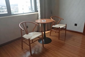 Una habitación con dos sillas de madera alrededor de una pequeña mesa redonda, una ventana con vistas y un interruptor de luz en la pared.