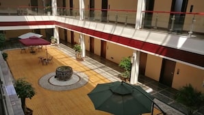A spacious indoor courtyard with a wooden floor, a round table, and several chairs. There are potted plants and a green umbrella. - Liangzhou Hotel (Luliang)