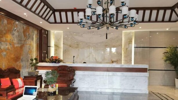 A lobby with a marble reception desk, wooden furniture, and a chandelier. - Liangzhou Hotel (Luliang)