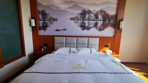 A hotel room with a large bed, a mural of a lake and mountains, and a wooden headboard. - Liangzhou Hotel (Luliang)