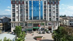 A multi-story hotel with a central entrance, surrounded by a parking area and greenery. - Liangzhou Hotel (Luliang)