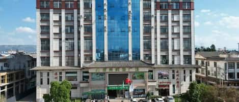 Un hotel de varios pisos con una entrada destacada, una bandera y varios coches estacionados frente.
