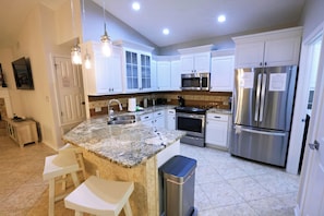 A modern kitchen with granite countertops, stainless steel appliances, white cabinetry, and pendant lighting. - Cozy Cottage! 5-Min Walk to Beach! Beachfront Pool, Hot Tub! Beach Service! (Destin)