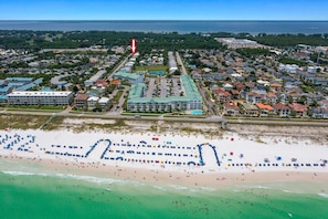 Ein Luftbild einer Küstenstadt mit Strand, Wohngebieten und einem großen Hotel mit mehreren Gebäuden und einem Schwimmbad.