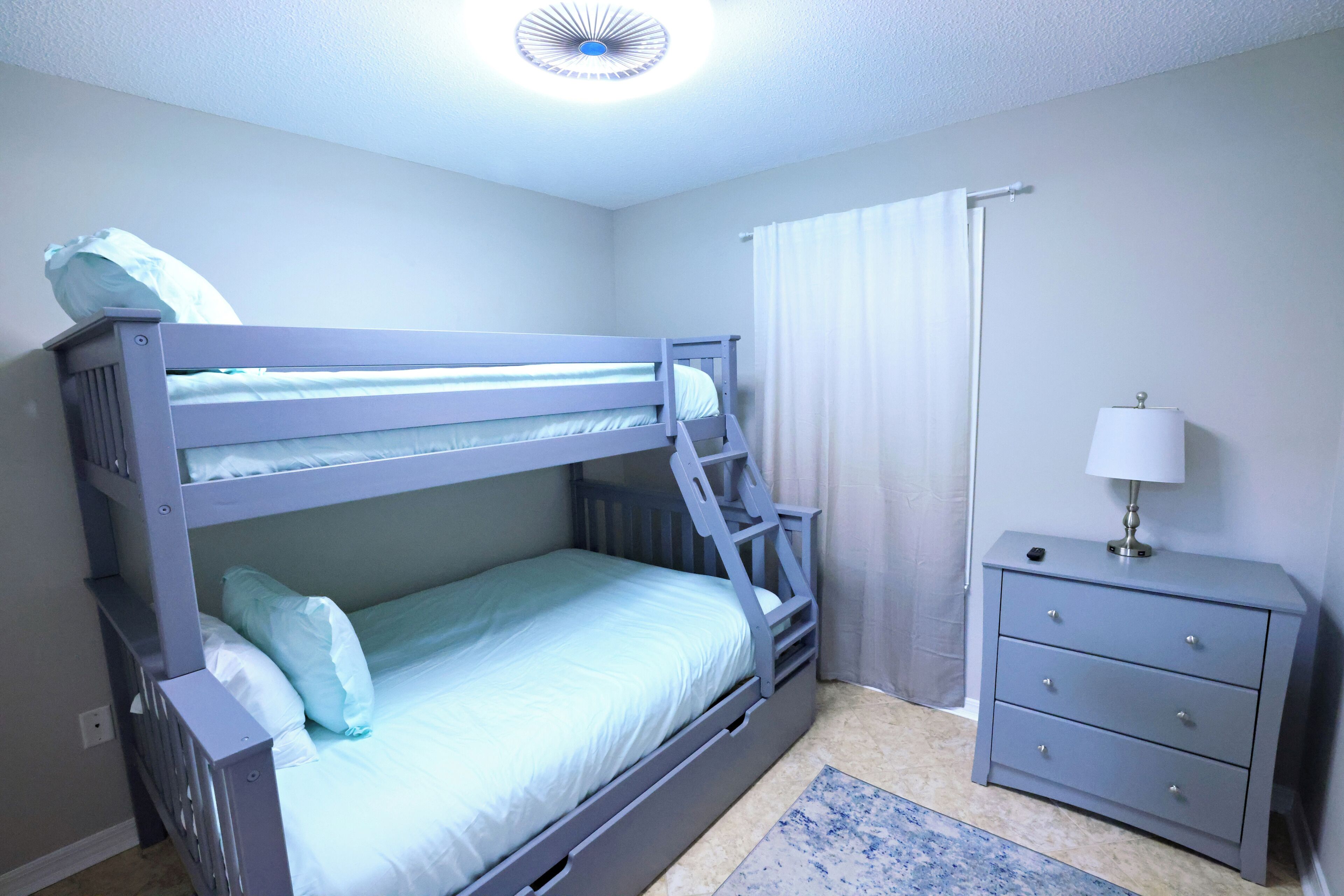 A bunk bed with a ladder, a bedside table with drawers, and a lamp.