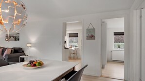 A modern living room with a dining area, featuring a white sofa, a dining table with fruit, and a pendant light.