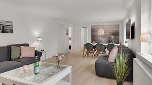 A modern living room with a sofa, a coffee table, and a dining area with chairs and a table.