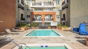 A rooftop pool with a view of a multi-story building, lounge chairs, and a warning sign.