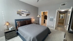 A bedroom with a bed, bedside tables, a ceiling fan, and a door leading to a bathroom.