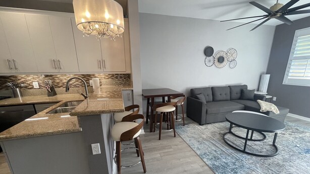 A modern kitchen with a central island, bar stools, a dining table, and a gray sofa in a living area.
