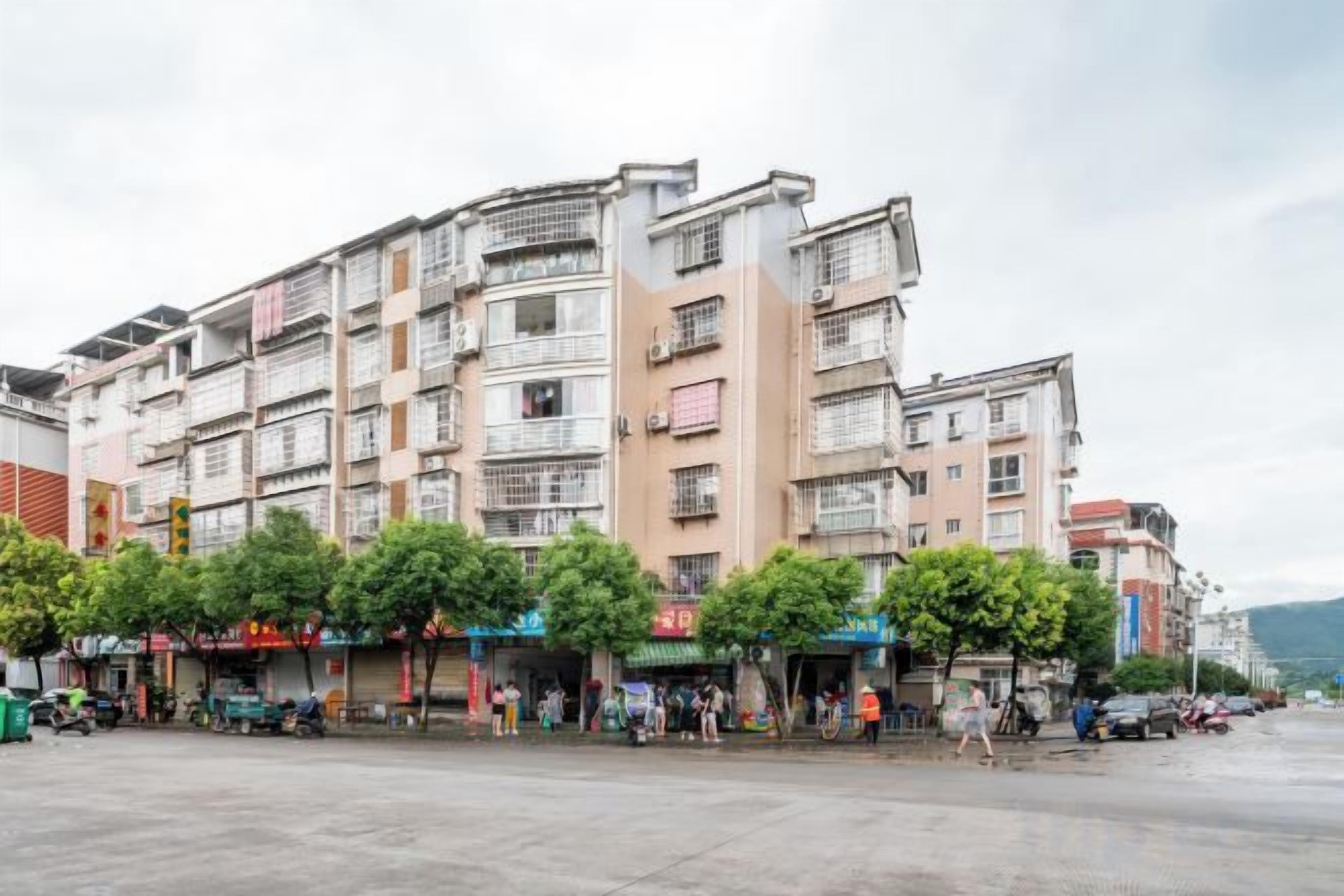 A multi-story building with balconies, a paved plaza, and storefronts.
