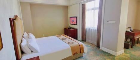 A hotel room with a bed, a desk, a television, and a window with curtains.