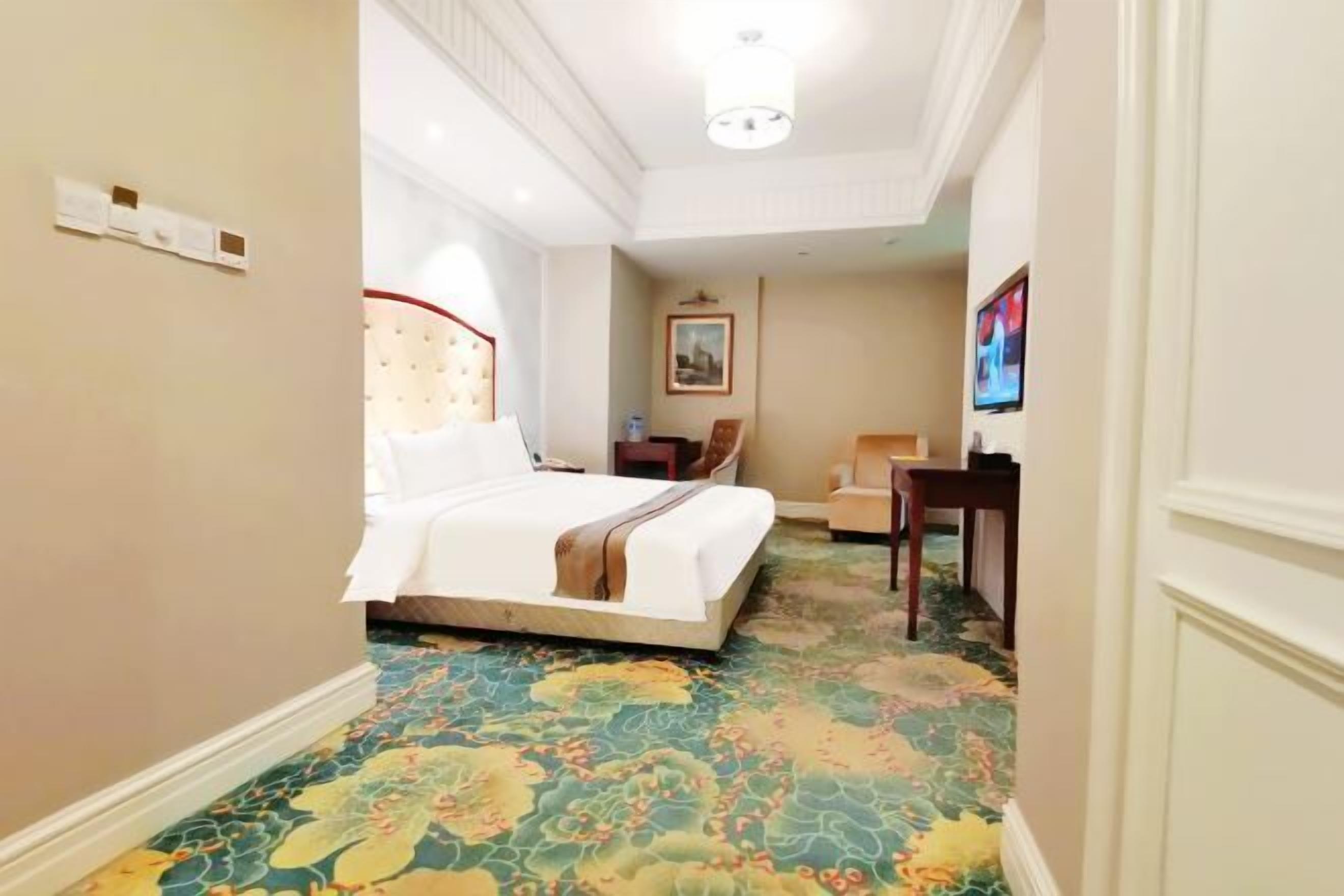 Ein Hotelzimmer mit Bett, Schreibtisch, Stuhl, Fernseher und einem Teppich mit Blumenmuster.