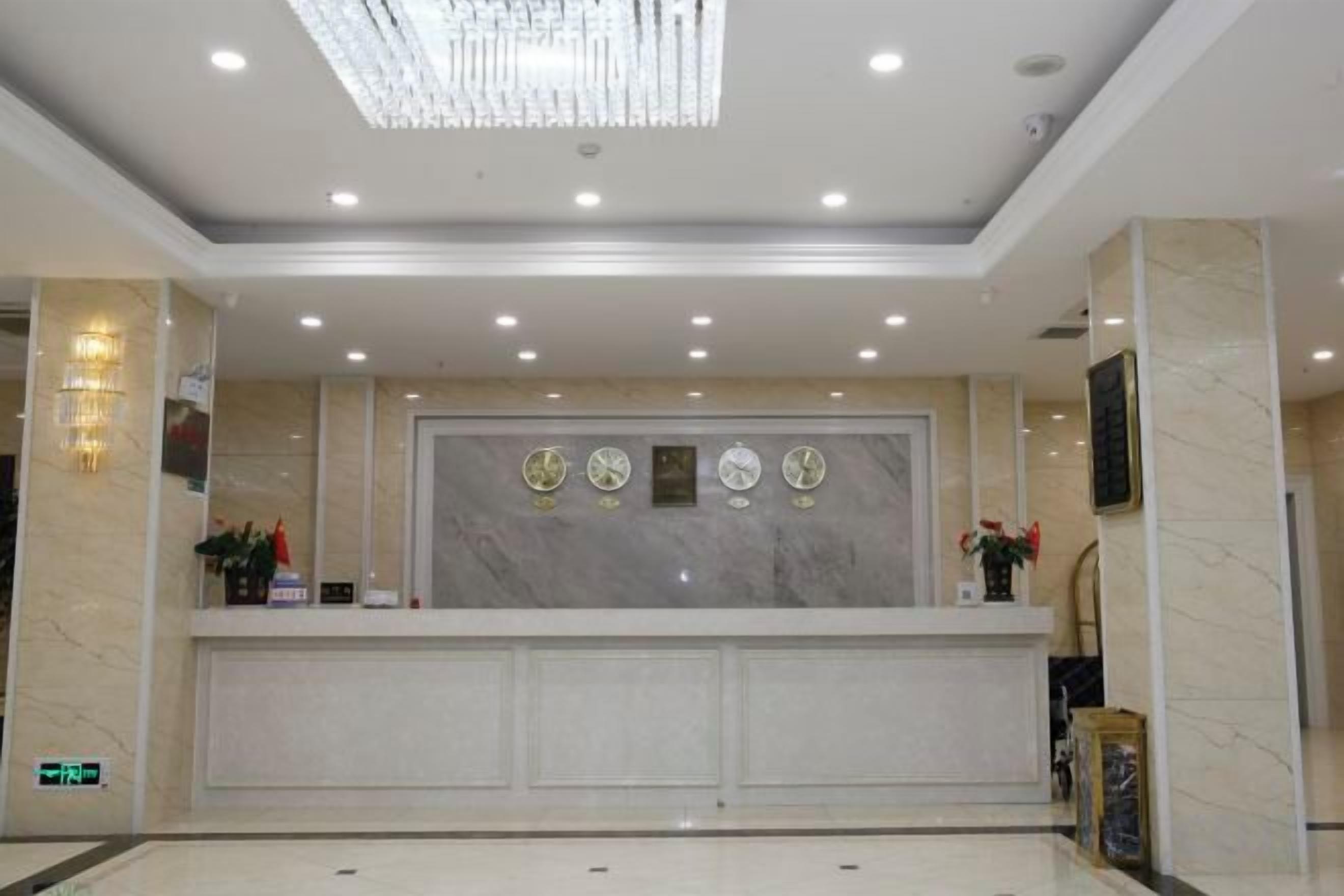 A hotel reception area with a marble counter, wall-mounted clocks, and a chandelier.