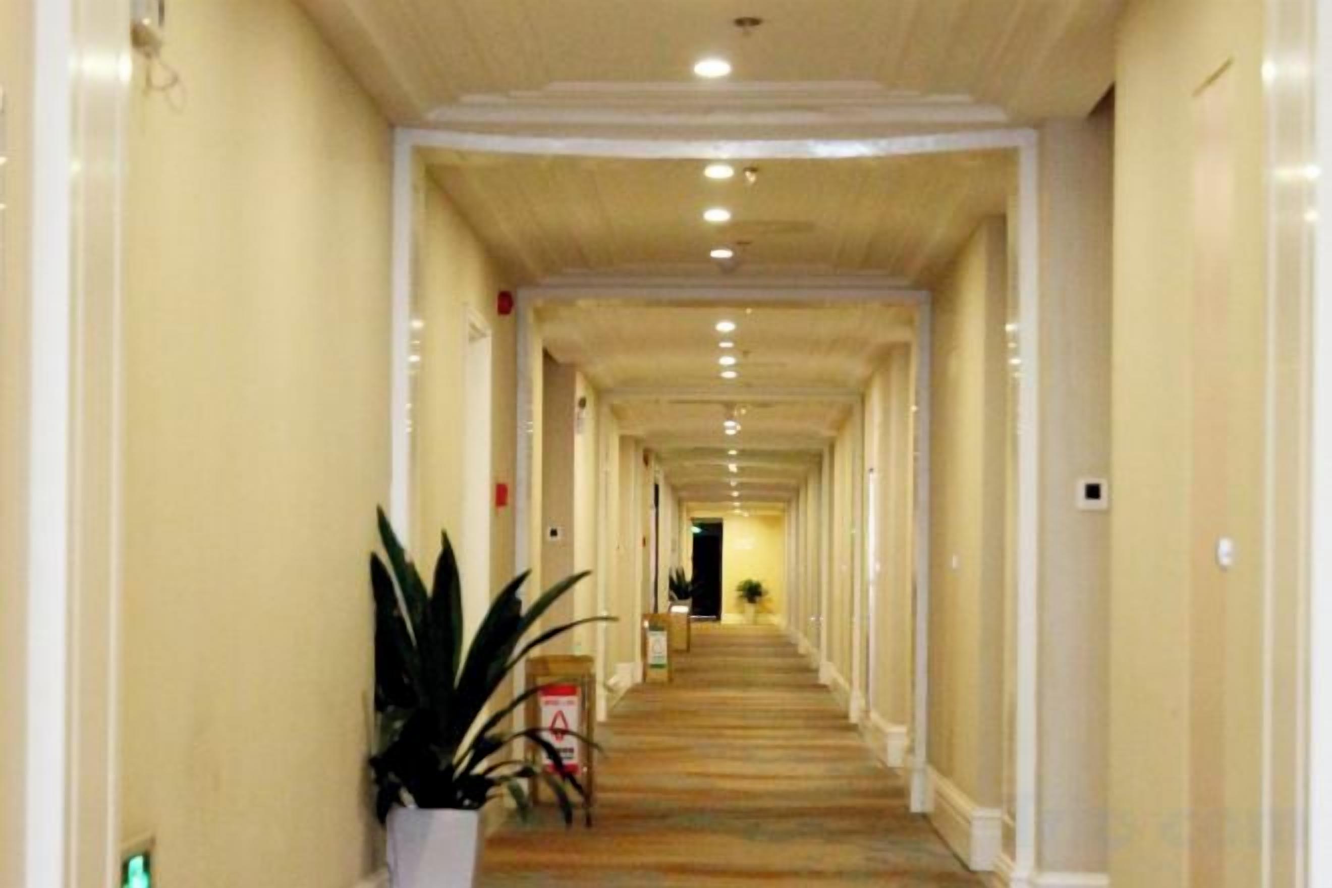 A long, narrow hotel corridor with a carpeted floor, white walls, and a ceiling with recessed lighting.