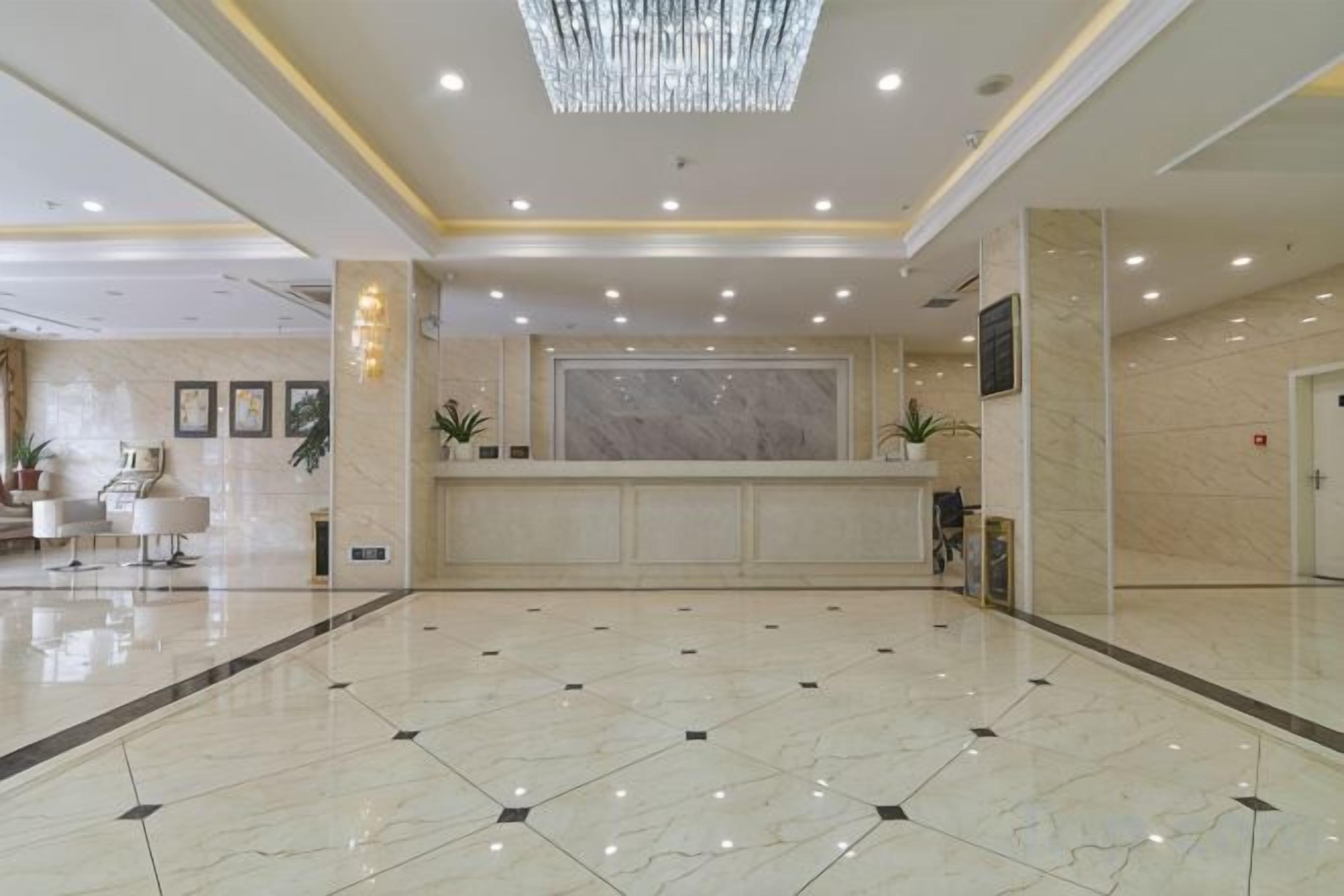 A hotel lobby with a reception desk, seating area, and a large chandelier.