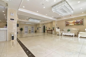 A hotel lobby with a reception desk, seating area, and a large painting on the wall.