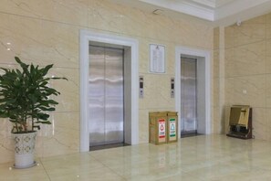 Two elevators in a lobby with a potted plant and boxes on the floor. - Anqing Yingdeli Hotel (Anqing)